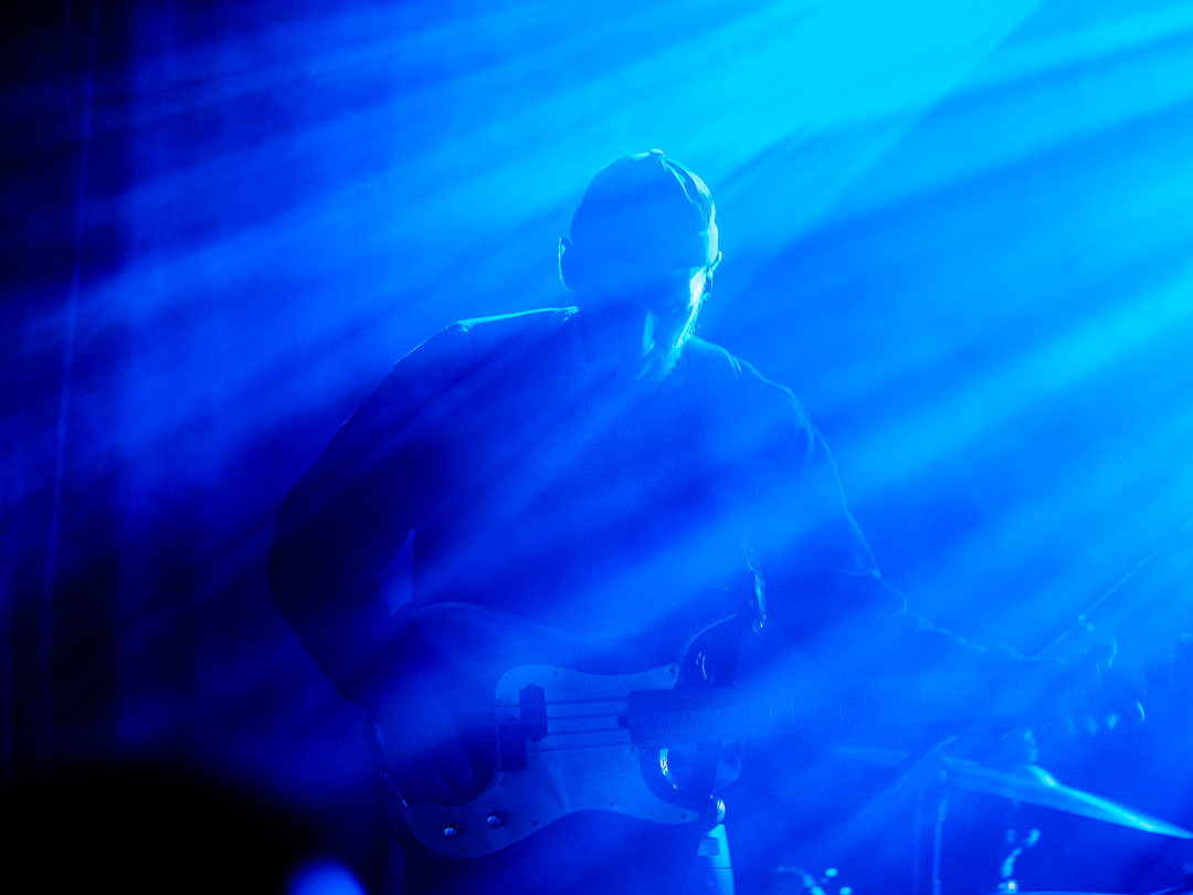 Lukas Pamminger von den Steaming Satellites spielt E-Bass im blauen Licht des Bühnenscheinwerfers.